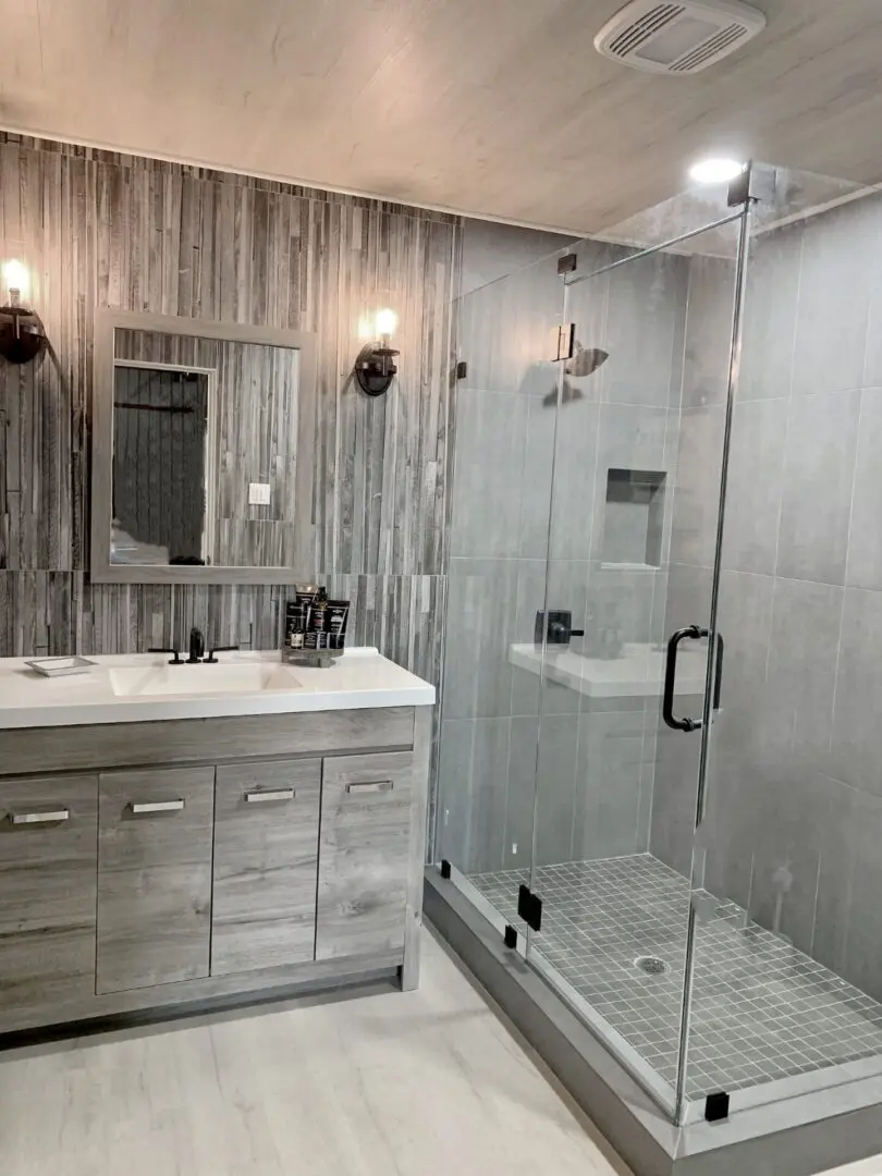 A bathroom with a glass shower stall and gray walls.