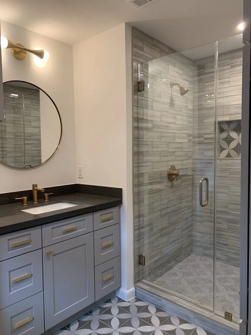 A bathroom with a glass shower stall and gray tile.