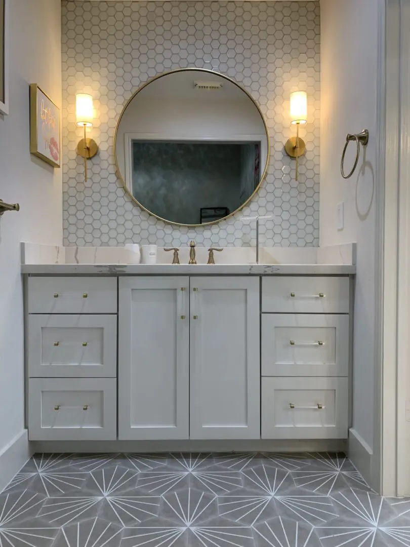 A bathroom with white cabinets and a round mirror.