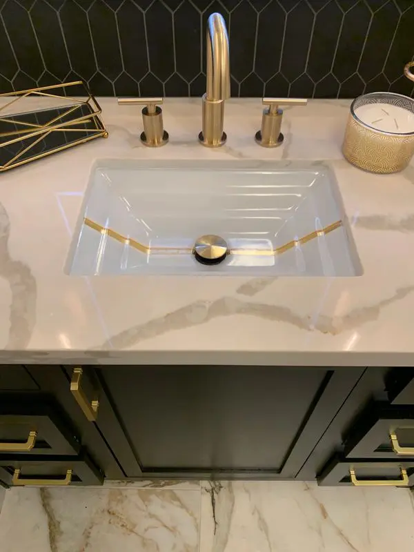 A black and gold bathroom with marble counter tops.