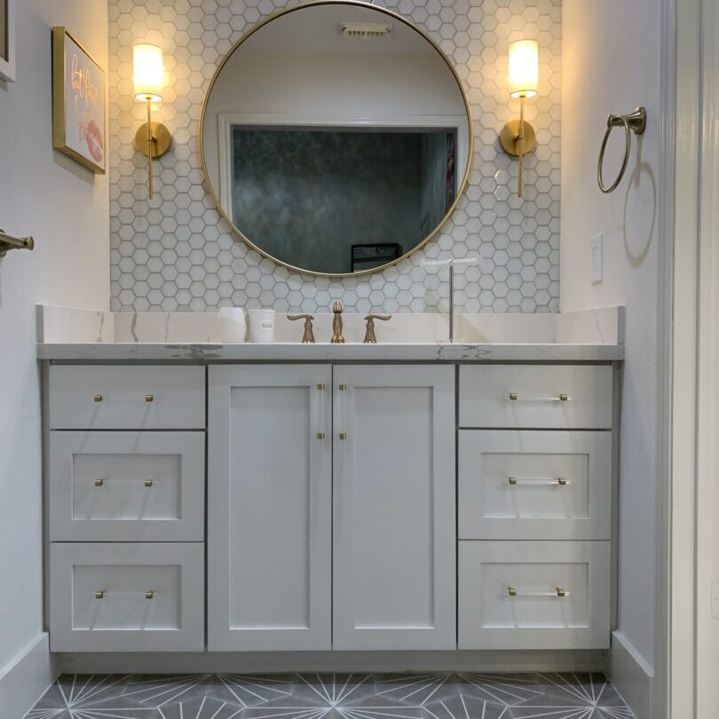 A bathroom with white cabinets and a round mirror boasting a modern design.